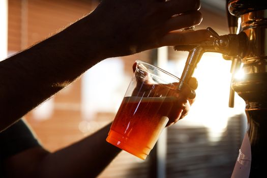 Pouring beer into a plastic glass. Sunset