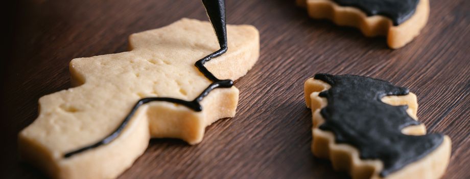 Close up of decorating cute Halloween bat gingerbread cookies with frosting icing cream topping bag.