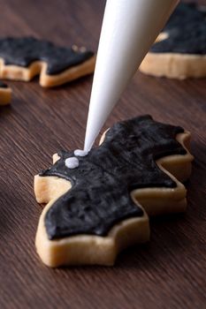 Close up of decorating cute Halloween bat gingerbread cookies with frosting icing cream topping bag.