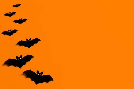 orange background with a flock of black paper bats for Halloween, black paper bat silhouettes on an orange background, Halloween concept, copyspace, flatlay, top view, overhead.