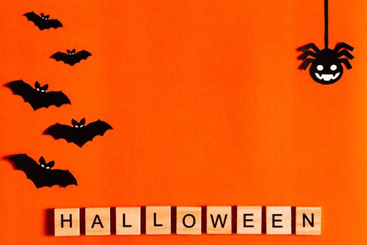 Halloween lettering on orange background with black paper silhouettes, bats, pumpkin, spider. The Concept Of Halloween. the view from the top.