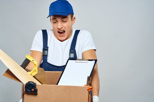 man in working uniform with a box in his hands tools loader delivery light background. High quality photo