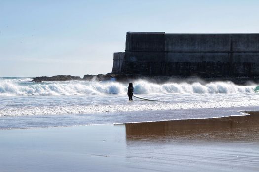 Beautiful beach called Praia da Torre in Lisbon, Portugal, in a sunny day of Spring. Surfers playing with the waves.