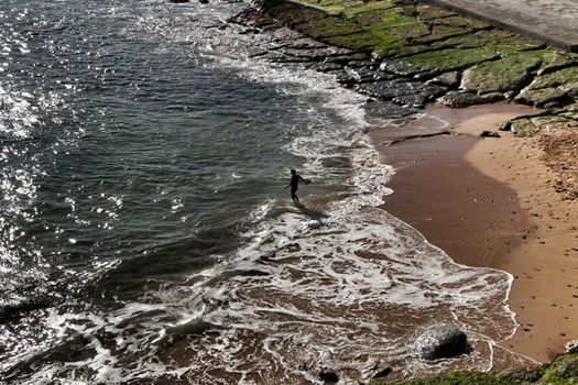 Surfer in the Beautiful Azarujinha beach with rock formations in Estoril, Lisbon, Portugal, in a sunny day of winter