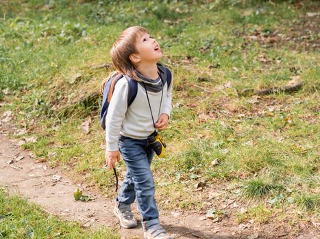 Little explorer on hike in forest. Boy with binoculars, backpack and rope. Outdoor leisure activity for children. Summer journey for young tourist.