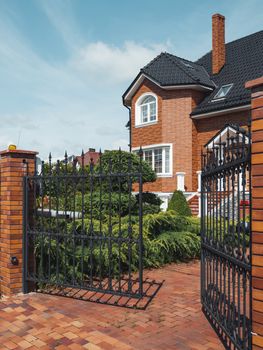 Gate is open to territory of house in suburbs of Kaliningrad. Well-kept brick building with manicured lawns. Russia.