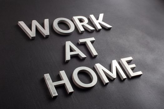 the words work at home laid with silver metal letters on matte black background in diagonal perspective, full frame view