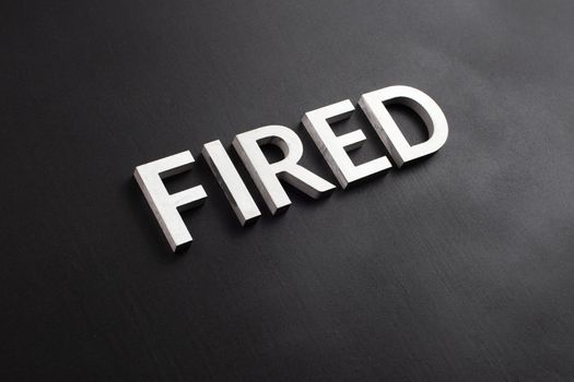 the word fired laid with white brushed metal letters on flat black surface in diagonal perspective with selective focus and background blur