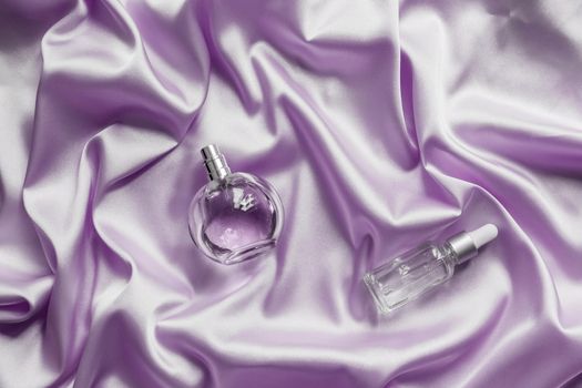 Perfume bottle and face serum on lilac silk folded fabric background. Luxery Scent fragrance cosmetic beauty product.
