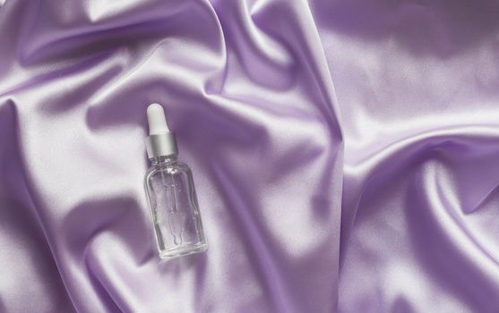 Face serum on lilac silk folded fabric background. Luxery cosmetic beauty product.