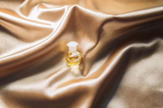 .Perfume bottle on gold folded silk fabric background. Luxery Scent fragrance cosmetic beauty product.