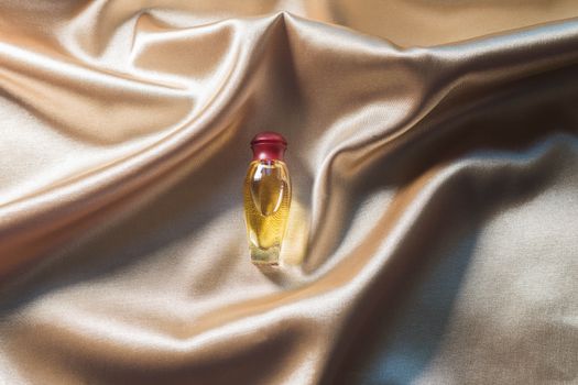 .Perfume bottle on gold folded silk fabric background. Luxery Scent fragrance cosmetic beauty product.