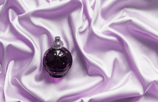 Perfume bottle on lilac silk folded fabric background. Luxery Scent fragrance cosmetic beauty product.