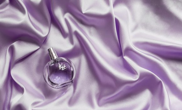 Perfume bottle on lilac silk folded fabric background. Luxery Scent fragrance cosmetic beauty product.