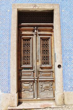 Old wooden door with tiled facade in Lisbon. Wrought metal details on the door.