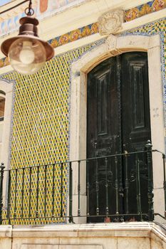 Old wooden door with tiled facade in Lisbon. Wrought metal details on the door.