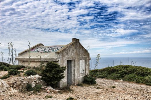 Old abandoned house in Cape Espiche, Portugal. Blue and cloudy sky.