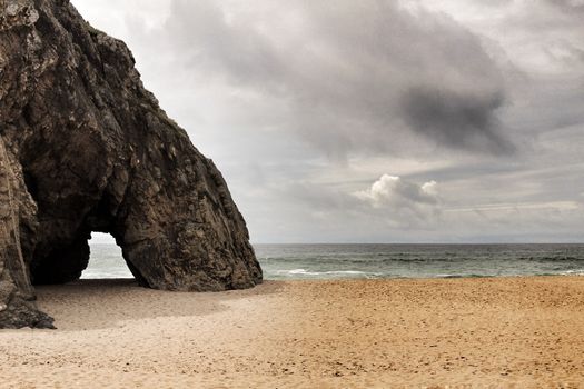 Brave ocean, rock formations and cloudy drama sky on the beach of Adraga in Sintra, Lisbon, Portugal
