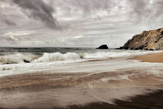 Brave ocean, rock formations and cloudy drama sky on the beach of Adraga in Sintra, Lisbon, Portugal