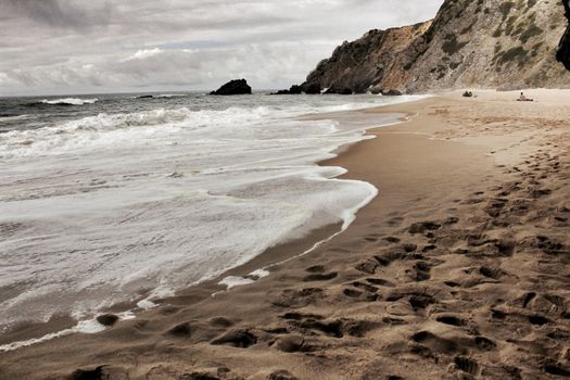 Brave ocean, rock formations and cloudy drama sky on the beach of Adraga in Sintra, Lisbon, Portugal