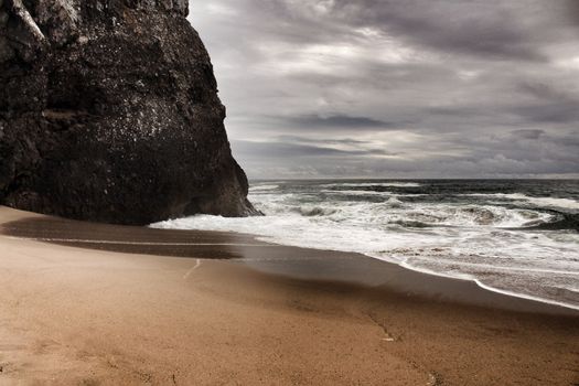 Brave ocean, rock formations and cloudy drama sky on the beach of Adraga in Sintra, Lisbon, Portugal