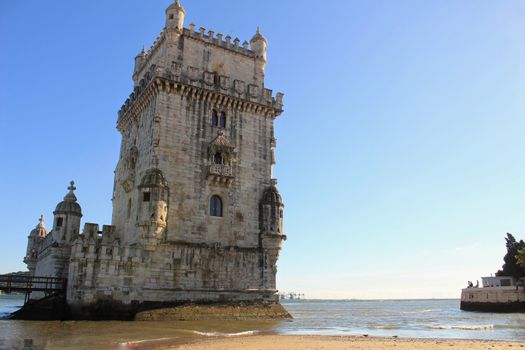 Belem tower and quiet Tagus river water in Lisbon under blue sky in the afternoon.