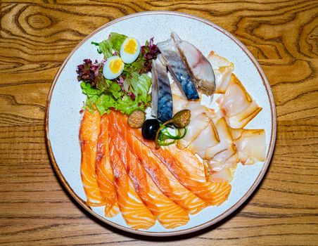 Dishes of herring, mackerel and red fish on a plate seasoned with quail egg and salad