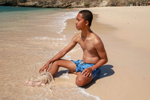 A young man sitting on the ocean and looks at the clear blue sea. Concept of good vacation.