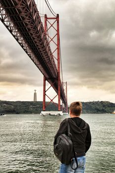 Lisbon, Portugal- June 1, 2018:Banks of the river Tagus in Lisbon in Spring on a cloudy day. Beautiful 25th April bridge structure. Woman looking at the river.