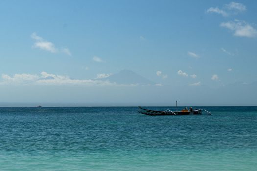 View of Rinjani volcano from Pink Beach Lombok. Bay with turquoise blue water and fishing boat anchored on calm sea level. Beach with its transparent water.