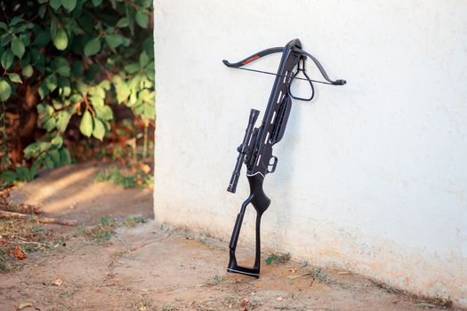 A black crossbow with a telescopic sight stands near the wall in the courtyard. Preparing weapons for hunting