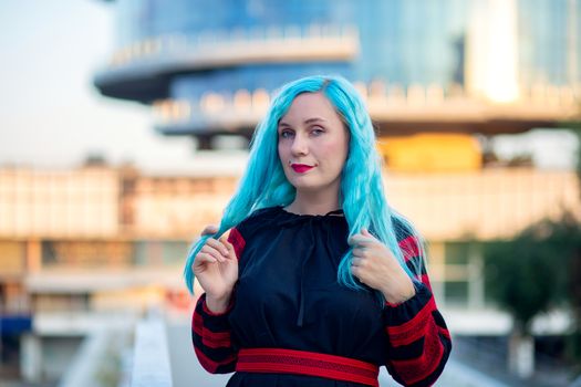 A woman with blue hair in a black dress walks through the city. Modern Informal with piercings and fashionable hairstyle