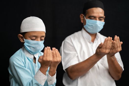 Muslim father and son in medical mask praying or performing Salah o protect from coronavirus or covid-19 by sitting