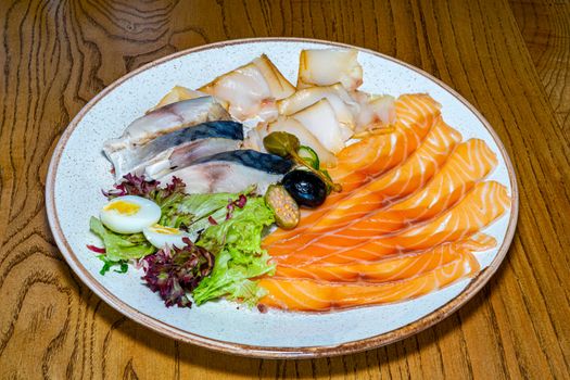 Dishes of herring, mackerel and red fish on a plate seasoned with quail egg and salad