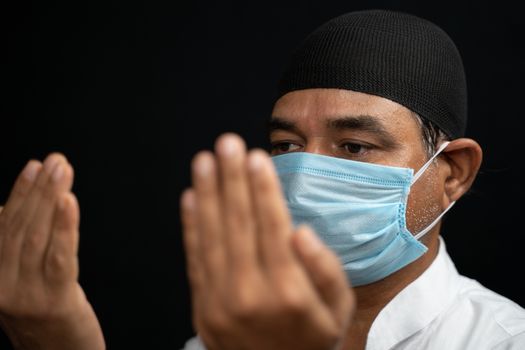 muslim man in medical mask preforming Salah or prayer by closing eyes