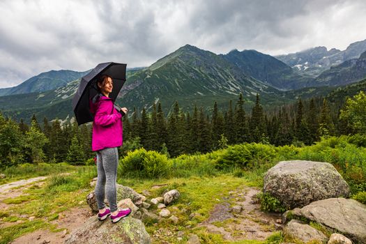 Beautiful mature woman with the umbrella in the rainy mountain scenery