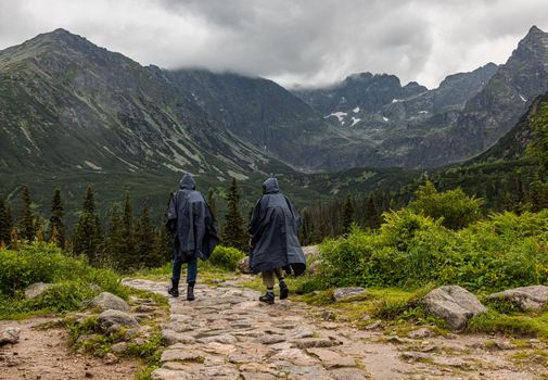 Two hooded hikers in parkas walking in the rain in Tatra mountains