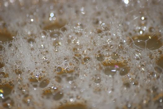 Closeup selective view of Foam and soap bubbles over water. white foam on water with brownish background