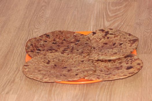 Traditional paratha - Macro closeup with selective focus of homemade oily bread or parotta on a plate on wooden floor. Chapati is traditional food of southeast Asia.