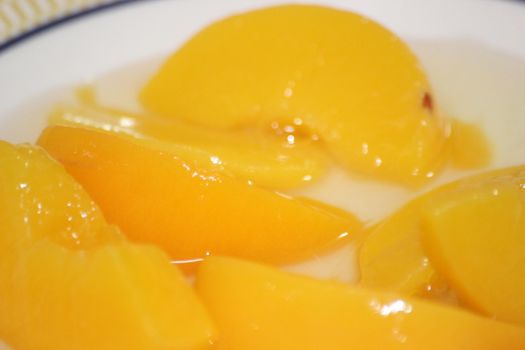 Closeup high angle view with selective focus of yellow peaches slices. Canned peaches halves sprinkled with syrup in white plate.