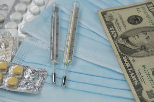 On the table is a thermometer, a pill, a medical mask, and money in dollars. The growth of prices for medicines in America in dollars.The United States is under quarantine of the epidemic coronavirus