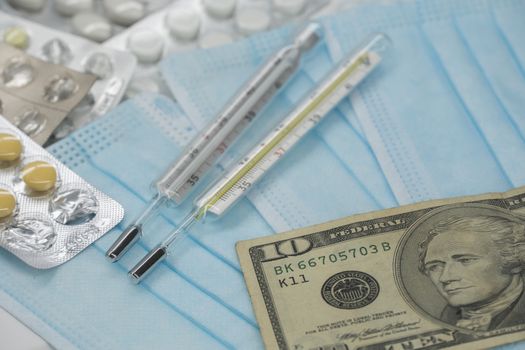 On the table is a thermometer, a pill, a medical mask, and money in dollars. The growth of prices for medicines in America in dollars.The United States is under quarantine of the epidemic coronavirus