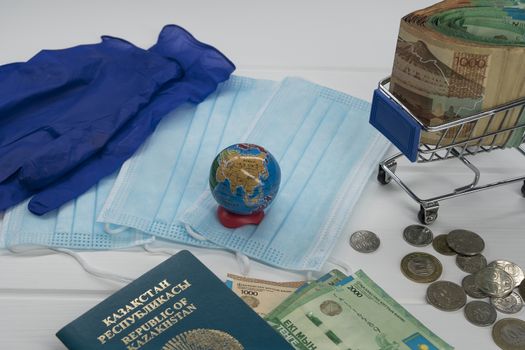 Quarantine in Kazakhstan. Tenge money with medical face masks, a globe, a card and a passport are on the table. The closure of borders and travel in Kazakhstan.