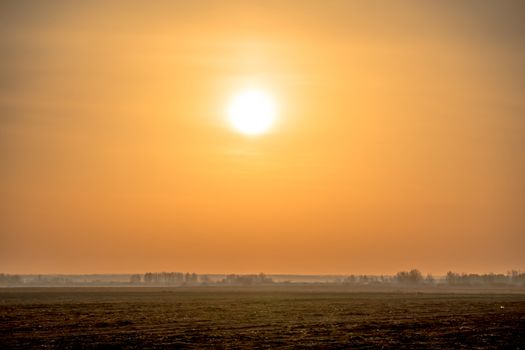 Sunrise over a plowed field in the Golden hour of summer. Close-up of the sun in the sky.