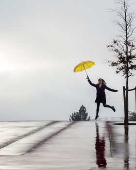 Woman jumping on the horizon with a yellow umbrella on a rainy day. Space for your text.