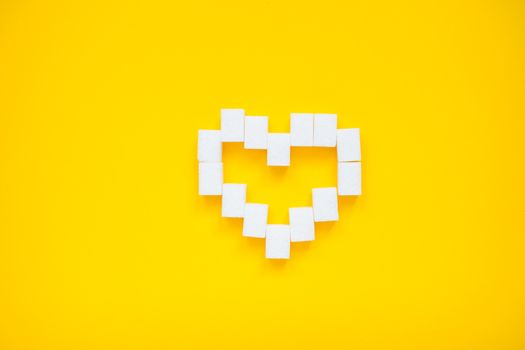 Heart made of pressed sugar cubes on a yellow background. Diabetes.