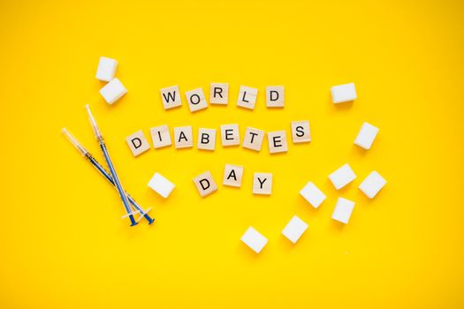 The inscription from wooden blocks world diabetic day and cubes of pressed sugar and insulin syringes on a yellow background. Diabetes.