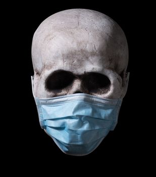 Human skull with a medical face mask isolated against a black background. Halloween image for the coronavirus pandemic era.