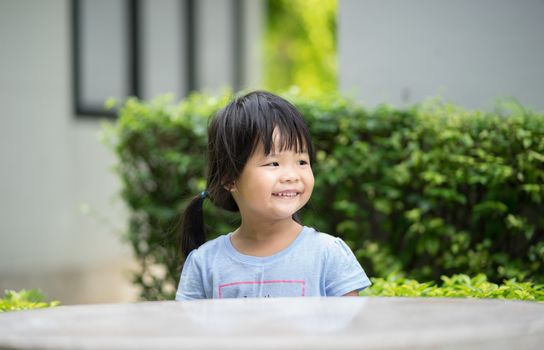 Little smiling girl in blue shirt sitting in the park