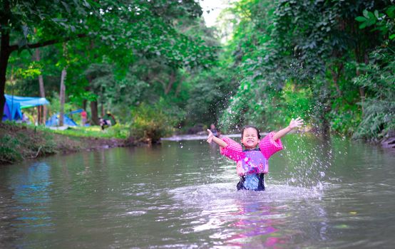 little asian girl wearing inflatable sleeves playing in nature water while camping on holiday